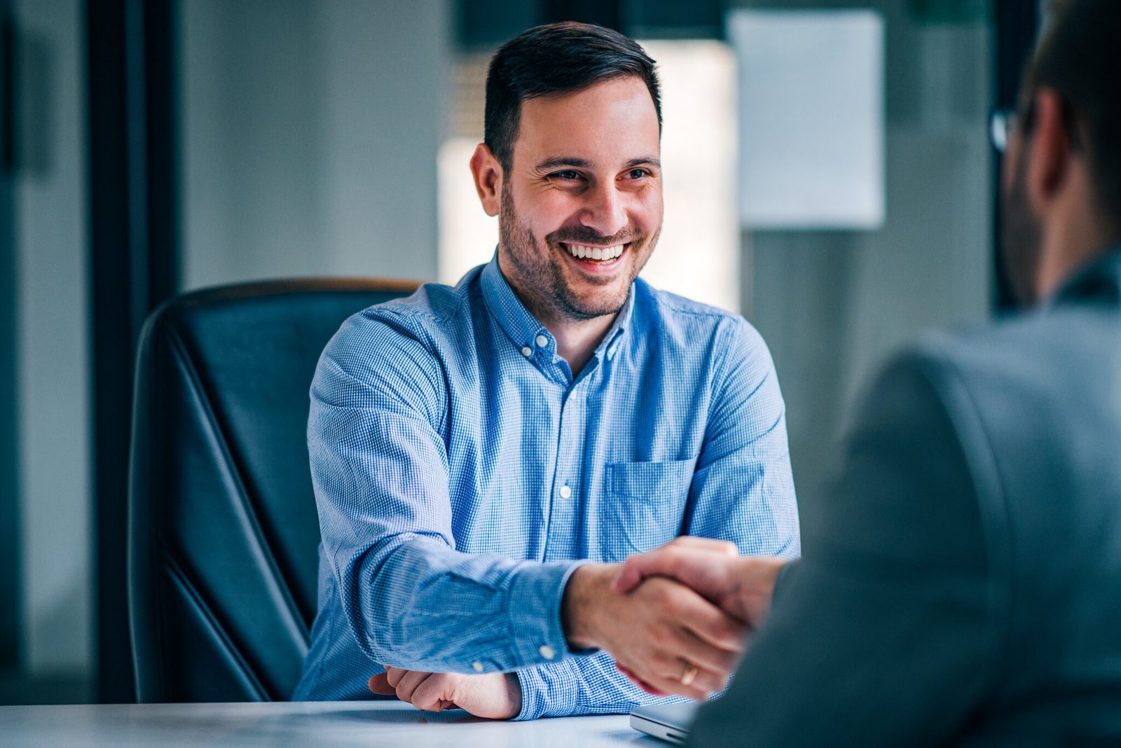 two smiling businessmen shaking hands while sitting at the offic